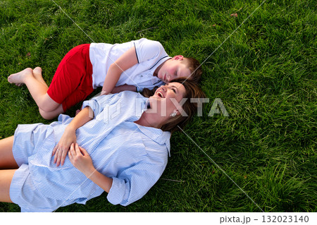 Boy naps beside laughing mother on evening park grass Boy naps beside laughing mother on evening park grass 132023140