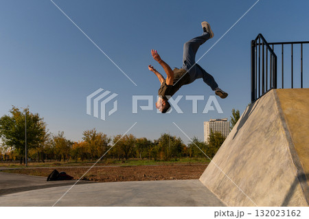 Freerunner launching into midair backflip from sloped wall outdoors 132023162