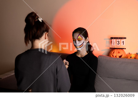 One person is getting their face painted for Halloween, while another person One person is getting their face painted for Halloween, while another person 132026009
