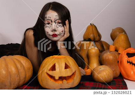 Woman with painted face surrounded by pumpkins, creating a festive Woman with painted face surrounded by pumpkins, creating a festive 132026021