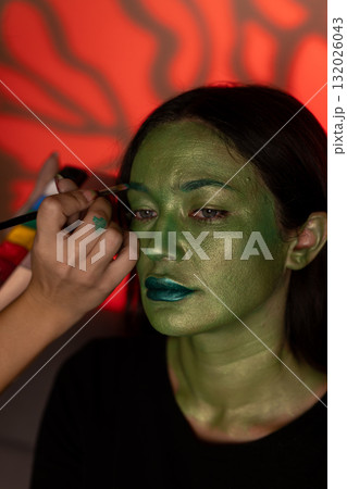 A person is getting their face painted green for a Halloween costume 132026043