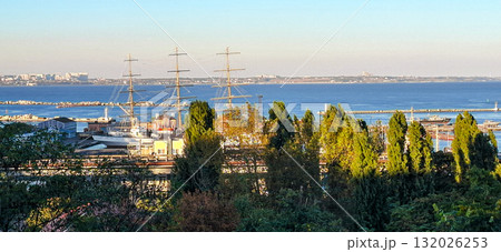 Panoramic view of a coastal harbor in Odessa, Ukraine, featuring tall ships with masts visible above the tree line in the foreground. Panoramic view of a coastal harbor in Odessa, Ukraine, featuring tall ships with masts visible above the tree line in the foreground. 132026253