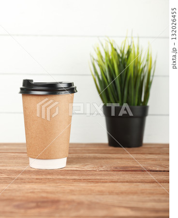 Disposable coffee cup standing on wooden table with decorative plant in background 132026455