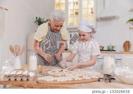 Happy family in kitchen. Grandmother granddaughter child cutting cookies of dough on kitchen table together. Grandma teaching kid girl cook bake cookies. Household teamwork helping family generations 132026638
