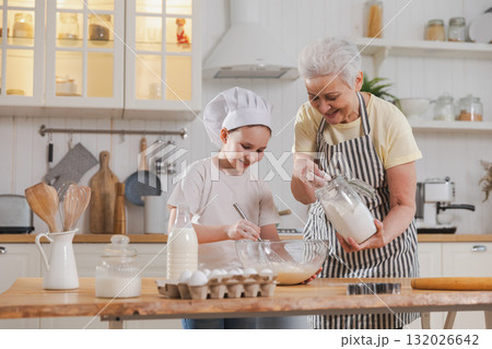 Happy family in kitchen. Grandmother and granddaughter child cook in kitchen together. Grandma teaching kid girl knead dough bake cookies. Household teamwork helping family generations concept Happy family in kitchen. Grandmother and granddaughter child cook in kitchen together. Grandma teaching kid girl knead dough bake cookies. Household teamwork helping family generations concept 132026642