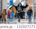 Happy funny person in Halloween grim reaper costume having fun in the mall holding shopping bags 132027173
