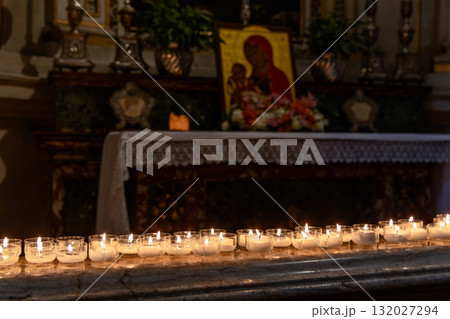 Glowing votive candles before altar with Madonna and Child icon create calm devotion Glowing votive candles before altar with Madonna and Child icon create calm devotion 132027294