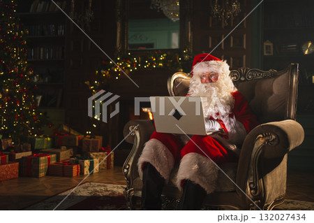 Merry Christmas. Santa Claus with laptop reading letters from children typing buying presents gifts online. Santa with computer on Christmas eve. Mail gifts of Santa Claus. Winter Holiday Celebrations 132027434