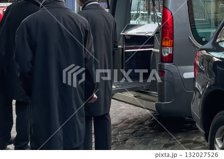 Men workers of funeral service loading the coffin into the hearse Men workers of funeral service loading the coffin into the hearse 132027526