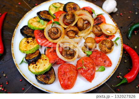 Grilled vegetables: red and yellow paprika, zucchini, eggplant, mushrooms, tomatoes and onions served on rustic wooden cutting board, white table background, top view 132027826
