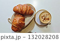Two golden croissants served on a ceramic plate with a cup of cappuccino sprinkled with cinnamon. Concept of cozy breakfast, comfort, and slow morning indulgence at home or cafe 132028208