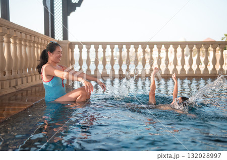 Mother Enjoying Water Play While Child Swims Joyfully Nearby Mother Enjoying Water Play While Child Swims Joyfully Nearby 132028997