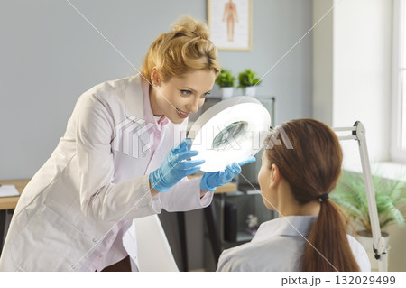 Dermatologist using magnifying lamp for patient skin examination in clinic Dermatologist using magnifying lamp for patient skin examination in clinic 132029499