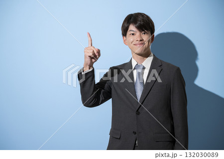 指差しをするスーツを着た若い新卒のようなビジネスマンのカメラ目線　就活などのイメージ　水色背景 132030089