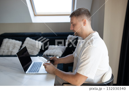 Man using laptop, smartphone and credit card for online payment at home Man using laptop, smartphone and credit card for online payment at home 132030340