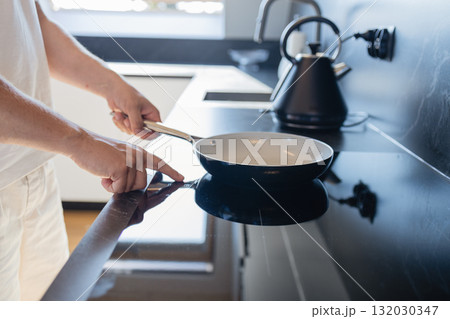 Man placing frying pan on modern electric stove in kitchen 132030347