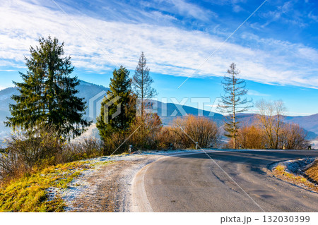 country road in carpathian mountains. beautiful landscape of ukraine in late autumn. fir trees on the roadside in morning light. scenic view of blue sky with clouds above the distant ridge in snow country road in carpathian mountains. beautiful landscape of ukraine in late autumn. fir trees on the roadside in morning light. scenic view of blue sky with clouds above the distant ridge in snow 132030399