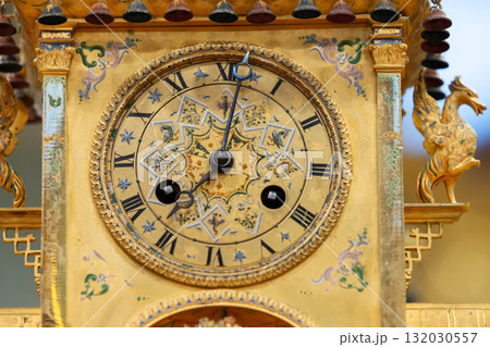 An ornate, gilded clock with Roman numerals and decorative patterns An ornate, gilded clock with Roman numerals and decorative patterns 132030557