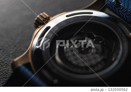 Back side of a bronze wrist watch resting on a textured fabric surface 132030562
