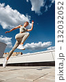 Athletic woman leaps in midair on a rooftop under a bright blue sky 132032052