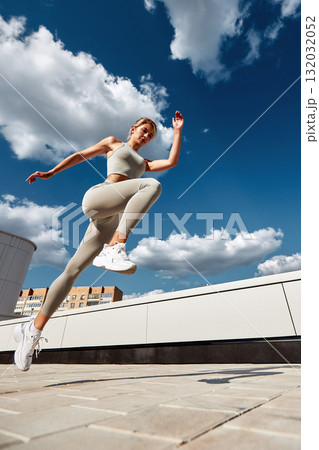 Athletic woman leaps in midair on a rooftop under a bright blue sky Athletic woman leaps in midair on a rooftop under a bright blue sky 132032052