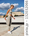 Woman in athletic wear performs rooftop stretch workout under blue sky and clouds 132032066
