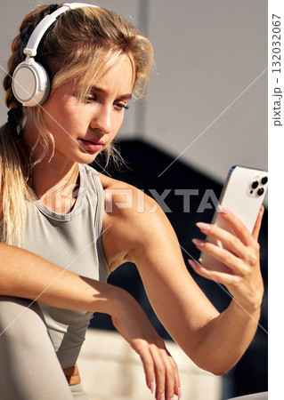 Woman wearing headphones takes a selfie with her phone during an outdoor workout session 132032067