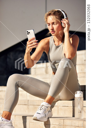 Athletic woman with headphones checking her phone on outdoor steps, ready for a workout 132032068