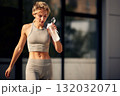 Athletic woman in a gray workout outfit drinks from a shaker bottle after a run outdoors 132032071