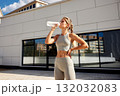 Athlete drinks protein shake after outdoor workout beside modern building, fitness training scene 132032083