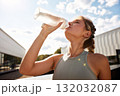 Athletic woman hydrating after workout outdoors on a sunny day in sportswear 132032087