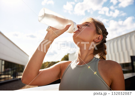 Athletic woman hydrating after workout outdoors on a sunny day in sportswear 132032087
