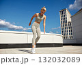 Athletic woman performs rooftop balance drill in gray activewear under a bright blue sky 132032089