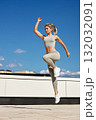 Strong athletic woman jumps in athletic wear on rooftop under clear blue sky during a sunny day 132032091