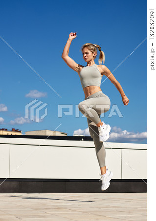 Strong athletic woman jumps in athletic wear on rooftop under clear blue sky during a sunny day 132032091