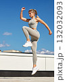 Athlete woman mid-air jump in athletic wear during outdoor rooftop workout against blue sky 132032093