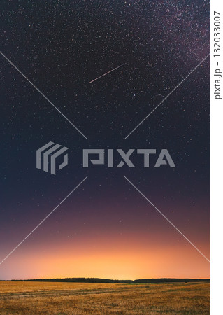 Natural Night Starry Sky Above Field Meadow. Glowing Stars, Meteorite Trail And Sunset Sunrise Lights Above Landscape In August Month. Meteoric Track In Night Sky Background 132033007