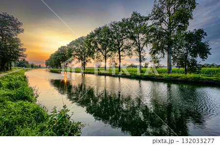 A Beautiful Serene Sunset Over a Tranquil Riverbank Surrounded by Lush Greenery and Nature 132033277
