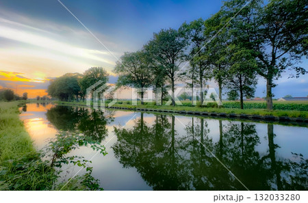 A Serene Sunset Reflection Along a Beautiful Tranquil Canal Surrounded by Lush Trees 132033280