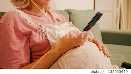 No face pregnant woman using phone and stroking her tummy. 132033489