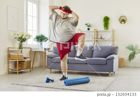 Overweight man lifting knees up and out to sides in funny home fitness workout Overweight man lifting knees up and out to sides in funny home fitness workout 132034133