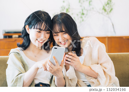 部屋でスマホを見る笑顔の女性2人組 部屋でスマホを見る笑顔の女性2人組 132034198