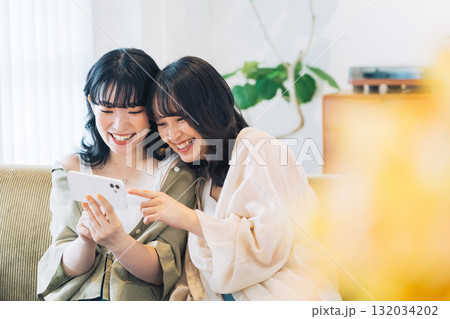 部屋でスマホを見る笑顔の女性2人組 132034202