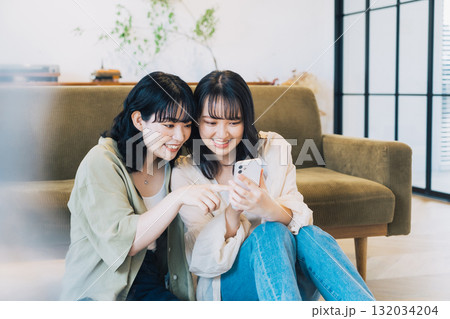 部屋でスマホを見る笑顔の女性2人組 132034204