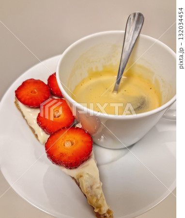 A cup of espresso with crema resting on a saucer with a slice of cake tart, topped with creamy white layer strawberries, creating an appetizing shot of a classic coffee and dessert pairing A cup of espresso with crema resting on a saucer with a slice of cake tart, topped with creamy white layer strawberries, creating an appetizing shot of a classic coffee and dessert pairing 132034454