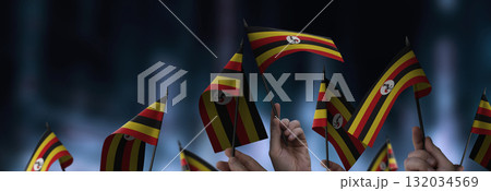 Uganda flags in their hands on a blurred urban background Uganda flags in their hands on a blurred urban background 132034569