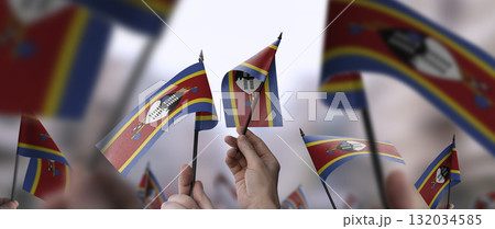 Swaziland flags in their hands on a blurred urban background Swaziland flags in their hands on a blurred urban background 132034585