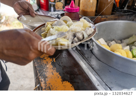 Traditional Indonesian street food vendor preparing Siomay, a popular steamed fish dumpling dish, for a customer. Traditional Indonesian street food vendor preparing Siomay, a popular steamed fish dumpling dish, for a customer. 132034627