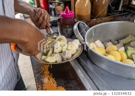 Traditional Indonesian street food vendor preparing Siomay, a popular steamed fish dumpling dish, for a customer. 132034632