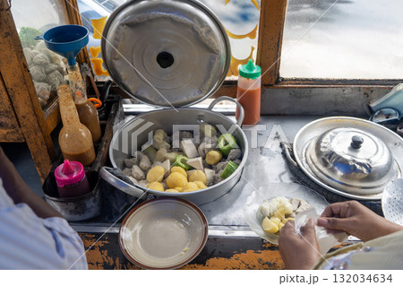 Traditional Indonesian street food vendor preparing Siomay, a popular steamed fish dumpling dish, for a customer. 132034634